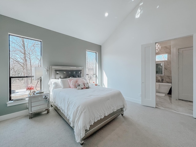 carpeted bedroom with ensuite bathroom, baseboards, and high vaulted ceiling