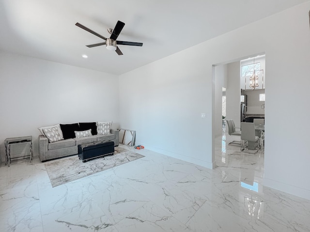 living area with ceiling fan with notable chandelier, baseboards, and marble finish floor