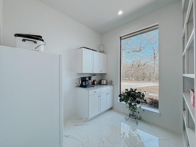 kitchen featuring white cabinets, freestanding refrigerator, a wealth of natural light, and marble finish floor
