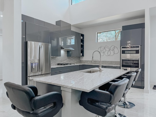 kitchen featuring stainless steel appliances, a kitchen breakfast bar, a sink, marble finish floor, and gray cabinets