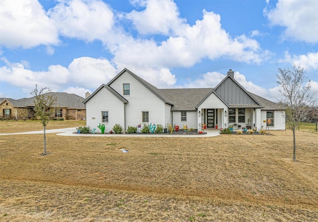 modern farmhouse style home featuring a chimney, a front yard, and board and batten siding