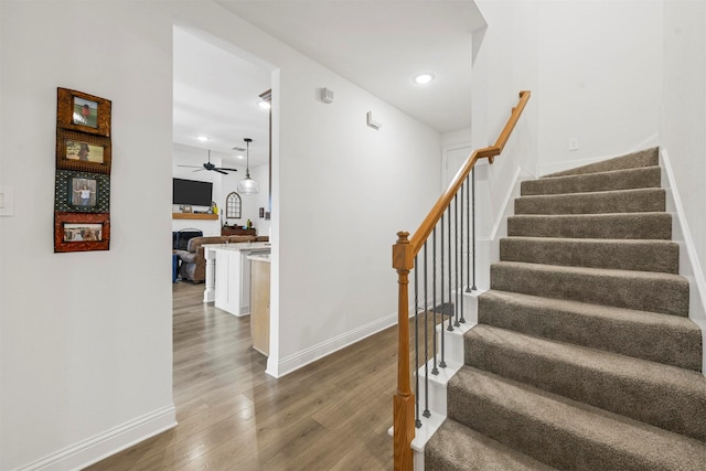 staircase with a fireplace, wood finished floors, a ceiling fan, and baseboards