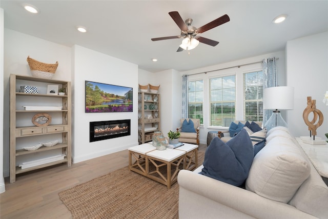 living area with light wood-type flooring, a glass covered fireplace, baseboards, and recessed lighting