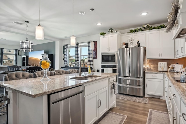 kitchen with white cabinets, wood finished floors, a kitchen island with sink, stainless steel appliances, and a sink