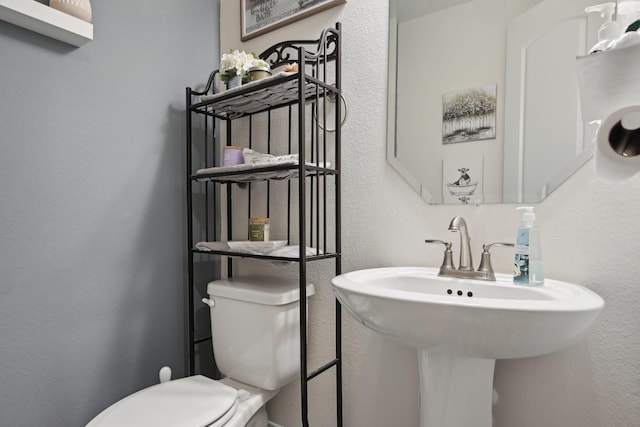 half bath featuring a textured wall, a sink, and toilet