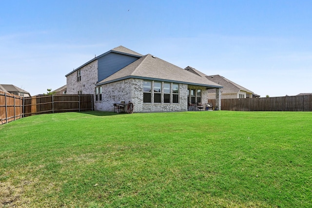 rear view of property with a fenced backyard, roof with shingles, a lawn, and brick siding