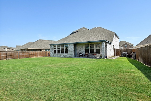 rear view of property featuring a fenced backyard, brick siding, a yard, roof with shingles, and a patio area