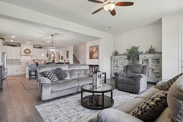 living area featuring stairs, light wood-type flooring, recessed lighting, and ceiling fan with notable chandelier