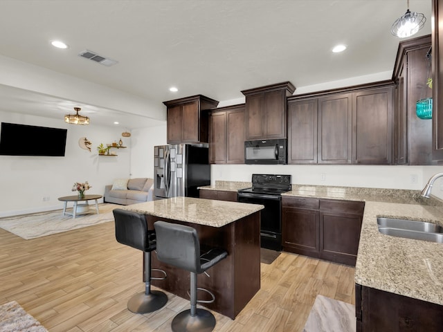 kitchen with visible vents, a kitchen island, a sink, black appliances, and light wood-style floors