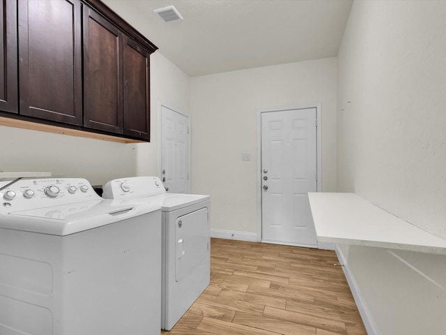 laundry area with visible vents, light wood-style flooring, washer and clothes dryer, cabinet space, and baseboards