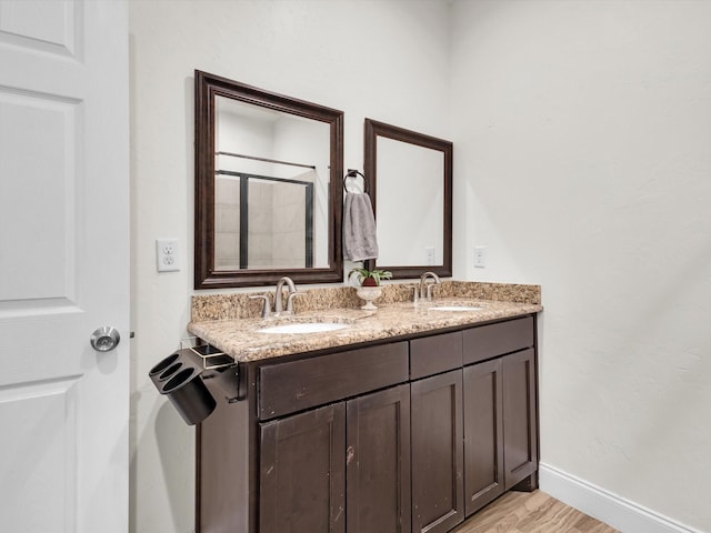 full bath featuring double vanity, wood finished floors, baseboards, and a sink