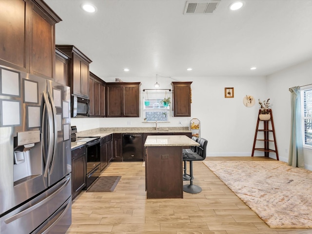 kitchen with visible vents, light wood-type flooring, black appliances, a sink, and a kitchen breakfast bar