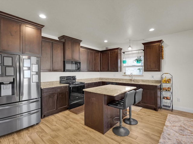 kitchen with a kitchen bar, black appliances, a kitchen island, light wood finished floors, and dark brown cabinets