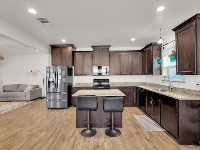 kitchen featuring visible vents, a sink, black appliances, dark brown cabinets, and a center island