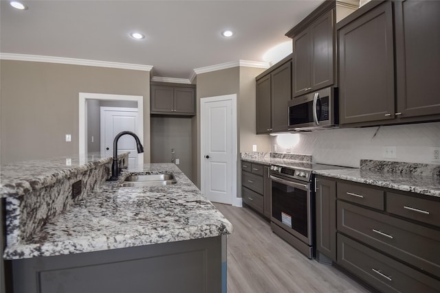 kitchen featuring crown molding, light stone counters, light wood-style floors, stainless steel appliances, and a sink