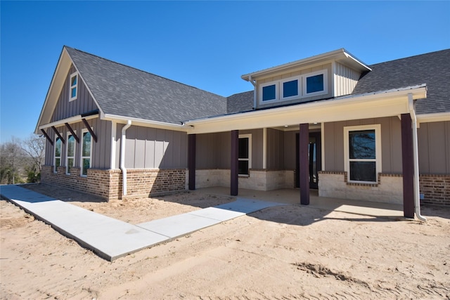 view of front facade with brick siding, board and batten siding, and a shingled roof