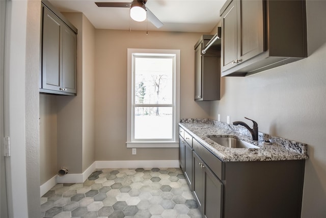 kitchen with a ceiling fan, light stone countertops, baseboards, gray cabinetry, and a sink