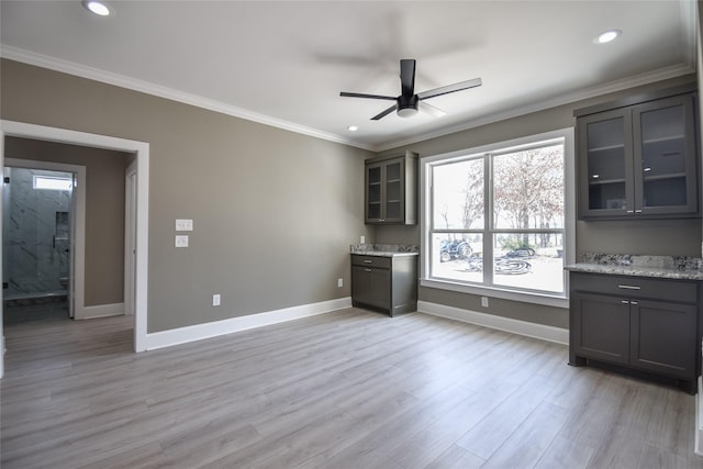 interior space featuring glass insert cabinets, light wood-style flooring, crown molding, and baseboards