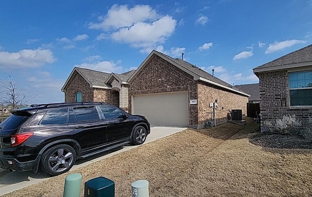 view of side of home with driveway, brick siding, an attached garage, and central air condition unit