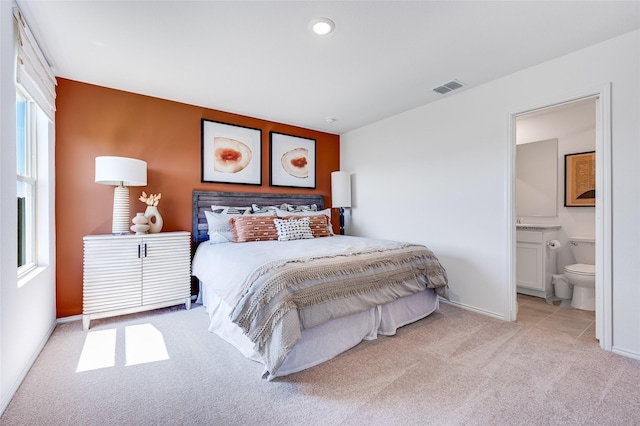 carpeted bedroom featuring ensuite bath, visible vents, and baseboards