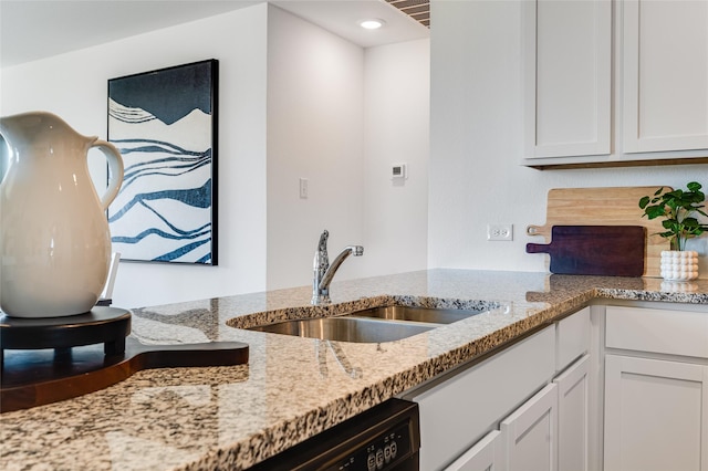 kitchen featuring black dishwasher, white cabinetry, light stone counters, and a sink