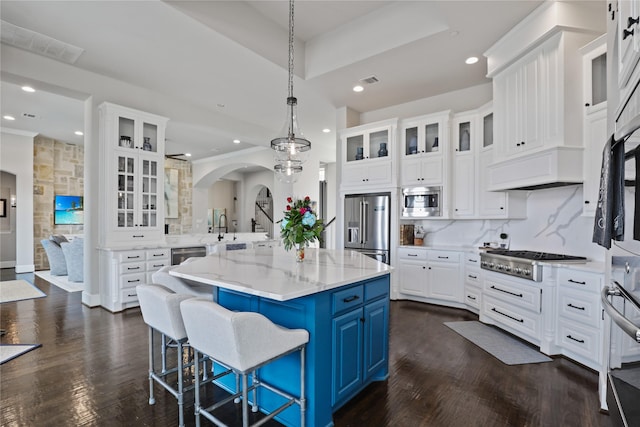 kitchen with tasteful backsplash, arched walkways, appliances with stainless steel finishes, blue cabinetry, and white cabinetry