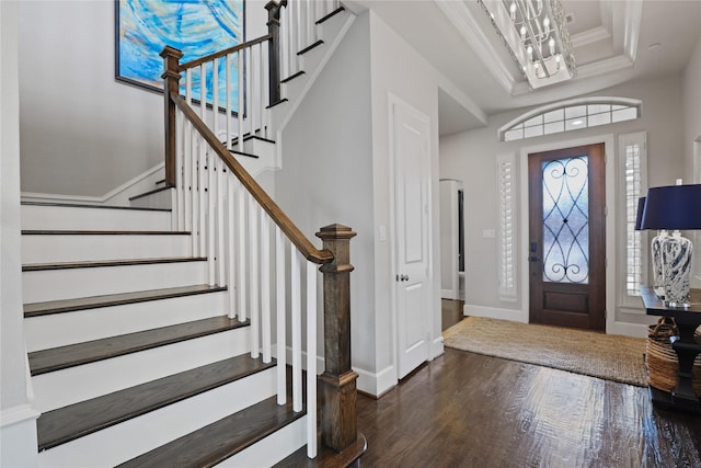 entryway featuring a notable chandelier, a raised ceiling, hardwood / wood-style floors, ornamental molding, and baseboards