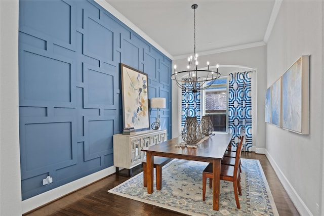 dining room with baseboards, dark wood-style floors, ornamental molding, a chandelier, and a decorative wall