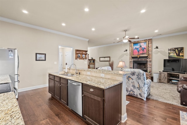 kitchen with dark brown cabinetry, appliances with stainless steel finishes, open floor plan, a fireplace, and a sink