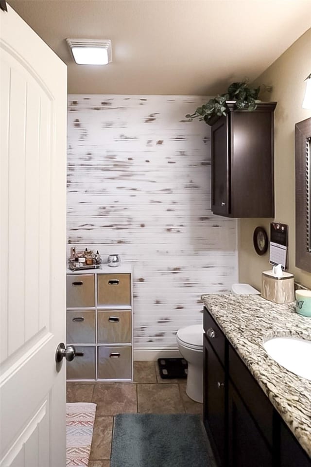 bathroom with baseboards, vanity, toilet, and wallpapered walls