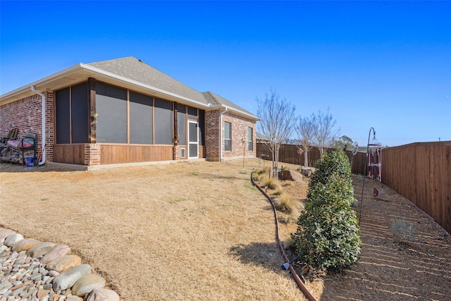 rear view of property with brick siding, roof with shingles, a fenced backyard, and a sunroom