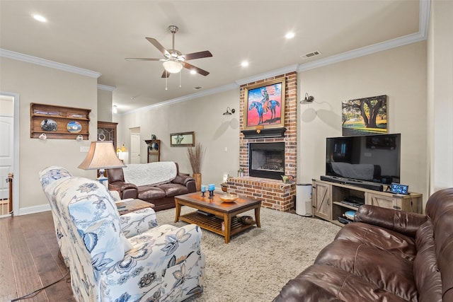 living area featuring visible vents, ceiling fan, ornamental molding, wood finished floors, and a brick fireplace