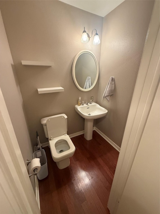 half bath featuring hardwood / wood-style floors, a sink, toilet, and baseboards