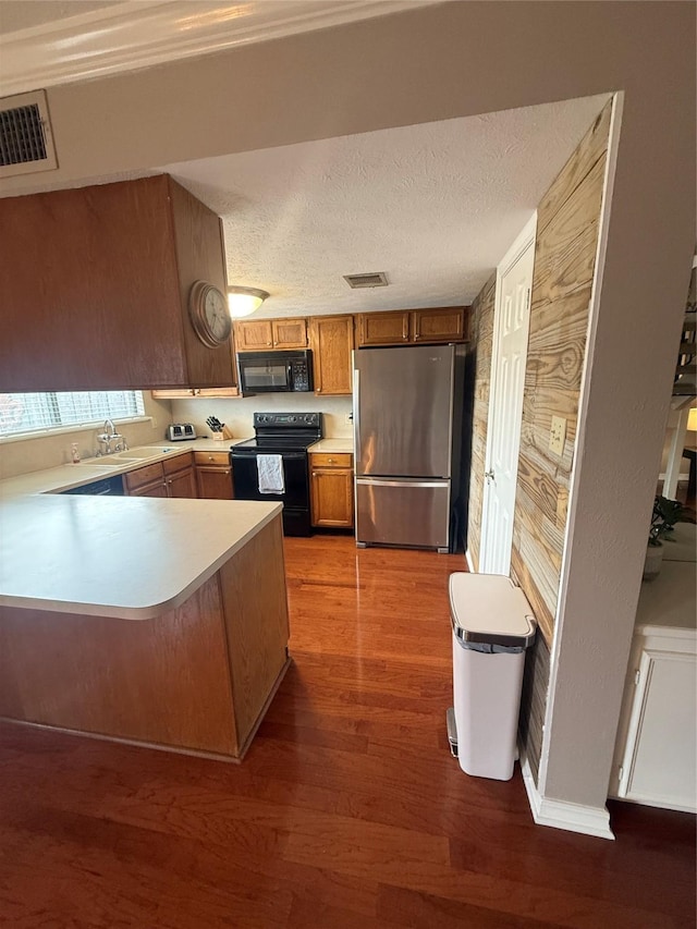 kitchen featuring a peninsula, visible vents, light countertops, black appliances, and brown cabinetry