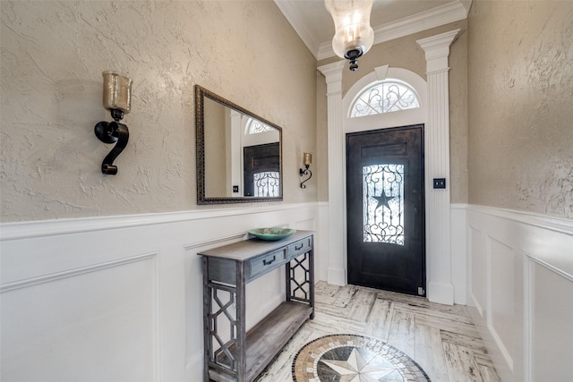 entrance foyer featuring a textured wall, decorative columns, crown molding, and wainscoting