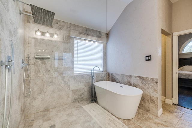 bathroom featuring tile walls, ensuite bathroom, vaulted ceiling, a freestanding tub, and walk in shower