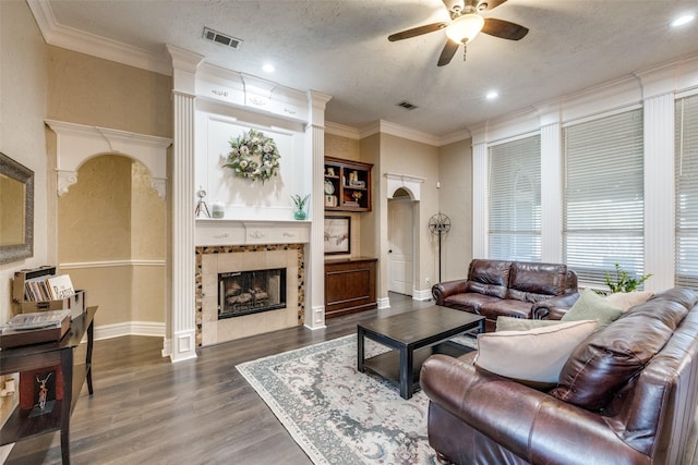 living room with visible vents, arched walkways, a tiled fireplace, wood finished floors, and crown molding