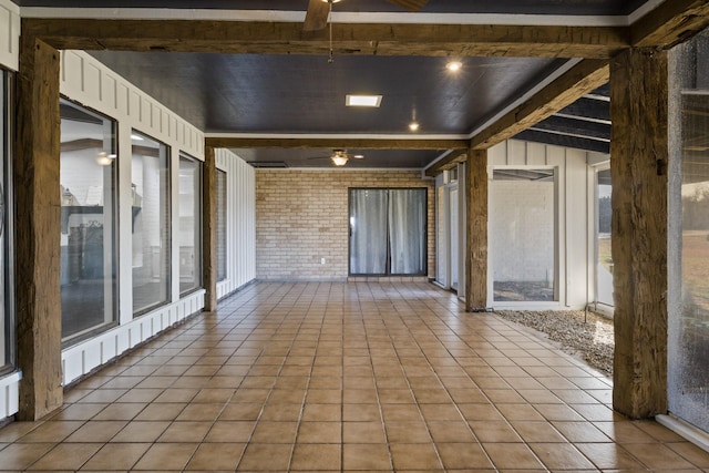 tiled spare room with brick wall, ceiling fan, a sunroom, and beamed ceiling