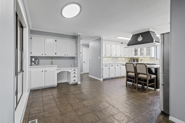 kitchen featuring white cabinets, light countertops, custom exhaust hood, built in study area, and tasteful backsplash