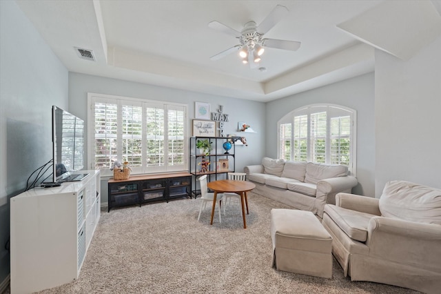 living area with a ceiling fan, a raised ceiling, visible vents, and light colored carpet