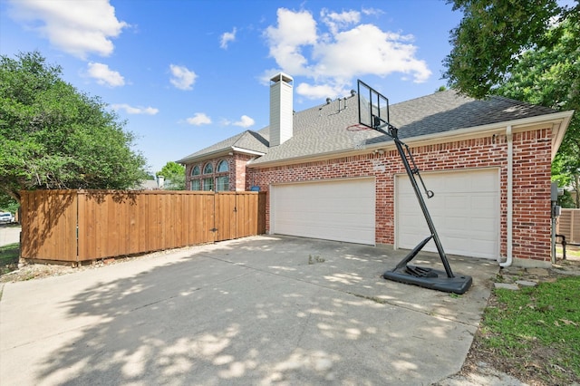 view of side of property featuring an attached garage, brick siding, a shingled roof, fence, and concrete driveway