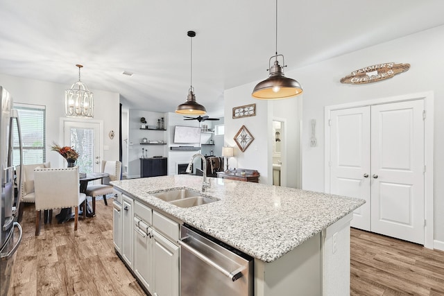 kitchen with decorative light fixtures, a sink, light stone countertops, light wood-style floors, and stainless steel dishwasher