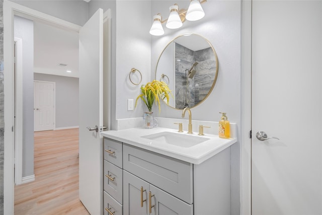 bathroom featuring baseboards, walk in shower, wood finished floors, and vanity