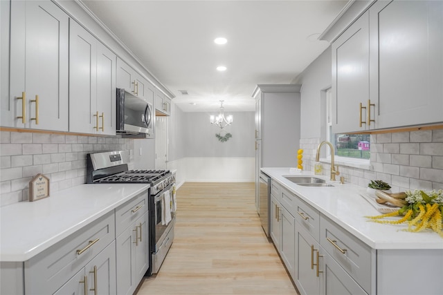 kitchen with gray cabinetry, stainless steel appliances, a sink, light countertops, and light wood finished floors