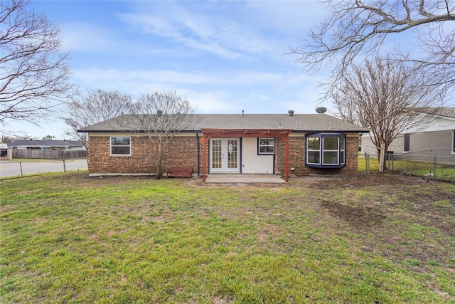 rear view of house with brick siding, a yard, fence, and french doors