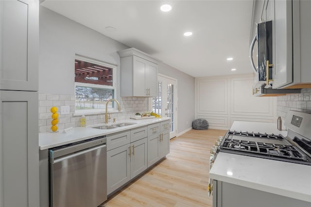 kitchen with stainless steel appliances, gray cabinets, a sink, and light wood-style flooring