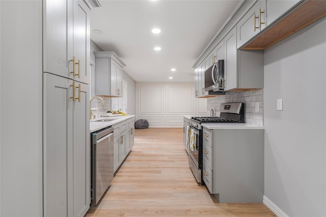 kitchen featuring stainless steel appliances, gray cabinets, light countertops, and light wood finished floors