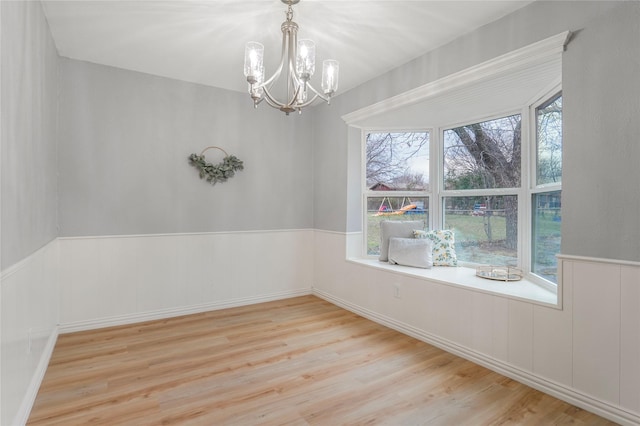 empty room featuring a wainscoted wall, a chandelier, and wood finished floors