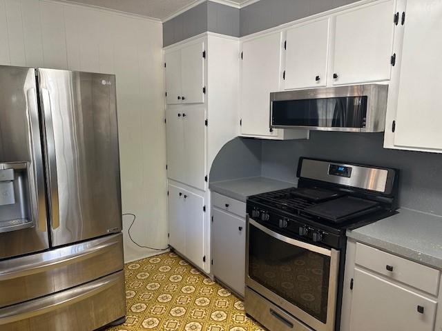 kitchen with appliances with stainless steel finishes, white cabinets, and crown molding