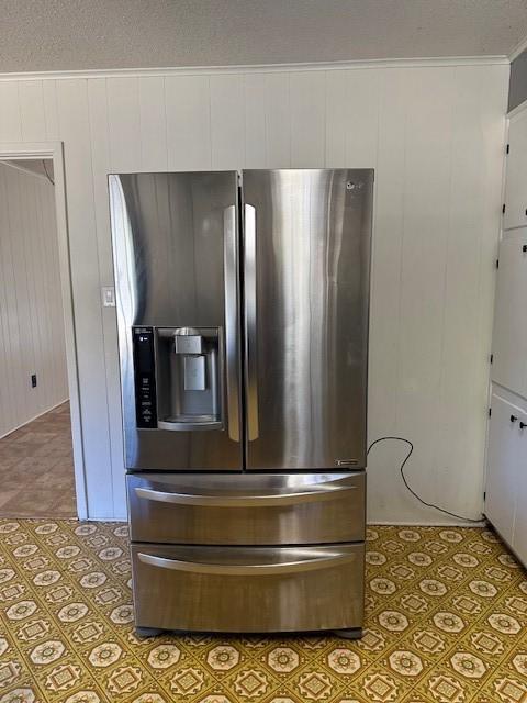 details with white cabinetry, crown molding, wooden walls, and stainless steel fridge with ice dispenser